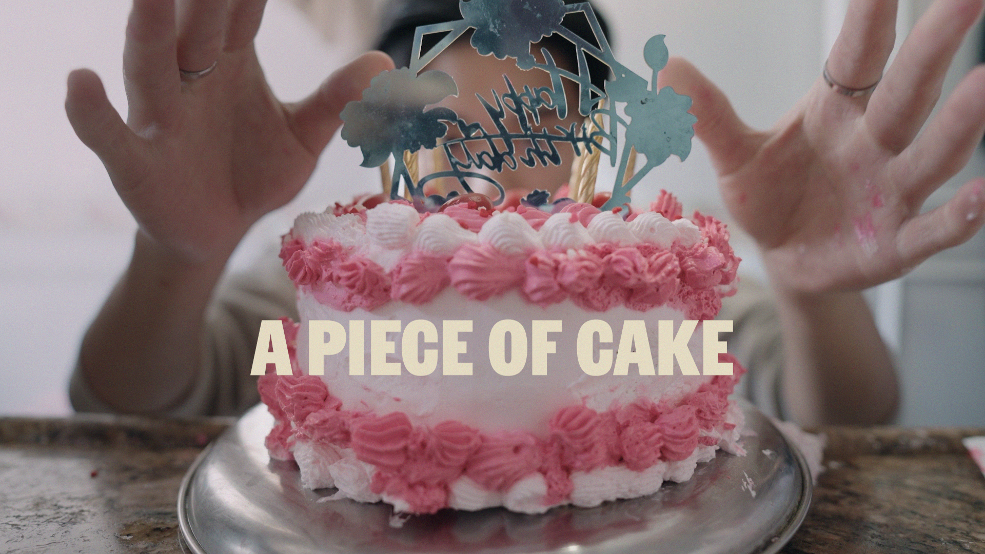 A mysterious baker tops a birthday cake with a flourish. The title 'A Piece of Cake' is superimposed on the still.